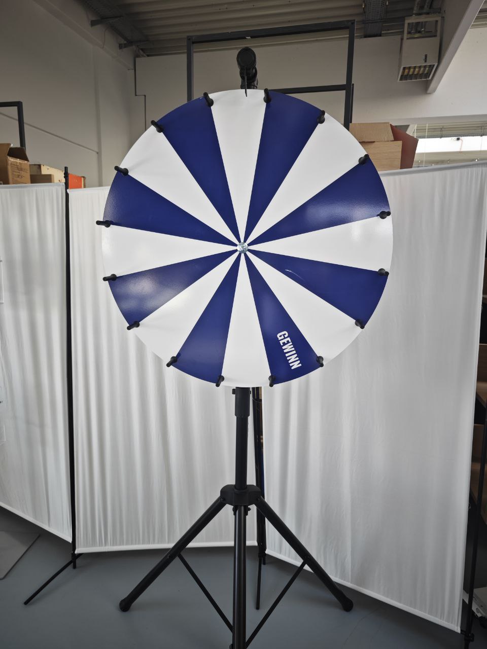 Blau-weißes Glücksrad mit 16 Segmenten und Aufschrift GEWINN auf schwarzem Stativ