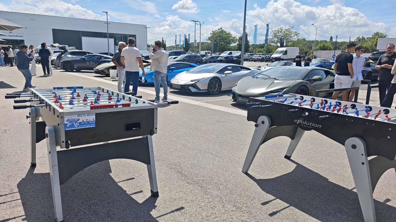 Zwei Wuzzler-Tische auf einem Autohaus-Vorplatz mit Supersportwagen