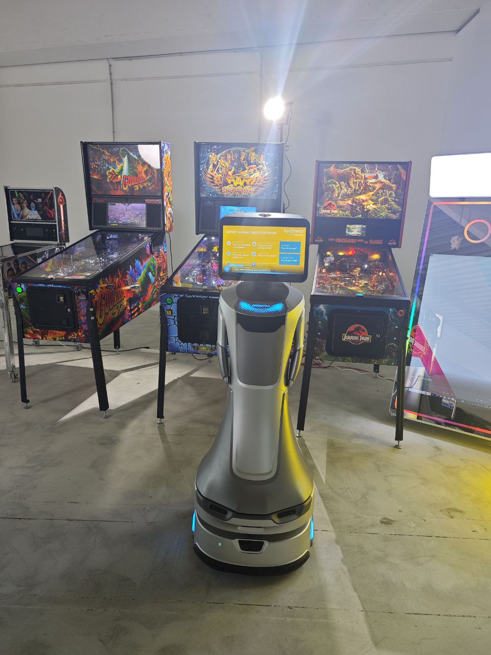 Servicerobot mit Display vor einer Reihe beleuchteter Flipperautomaten